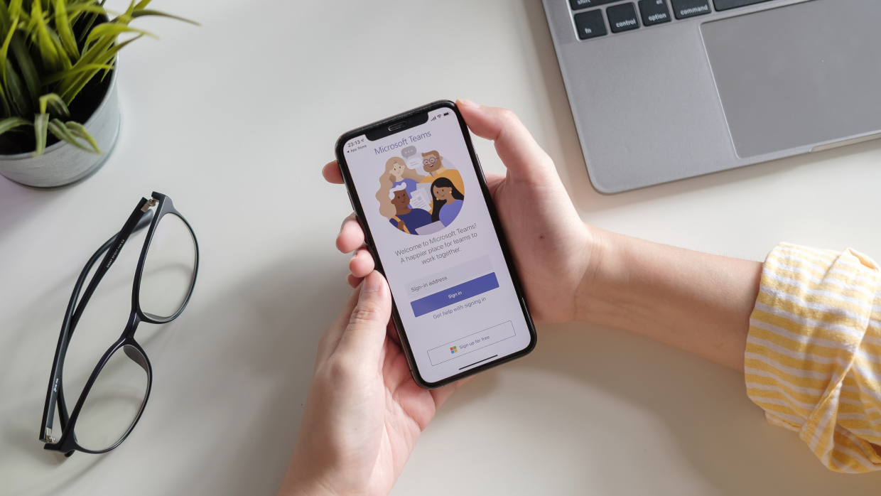 Person holding a mobile phone with the Microsoft Teams login page on the screen