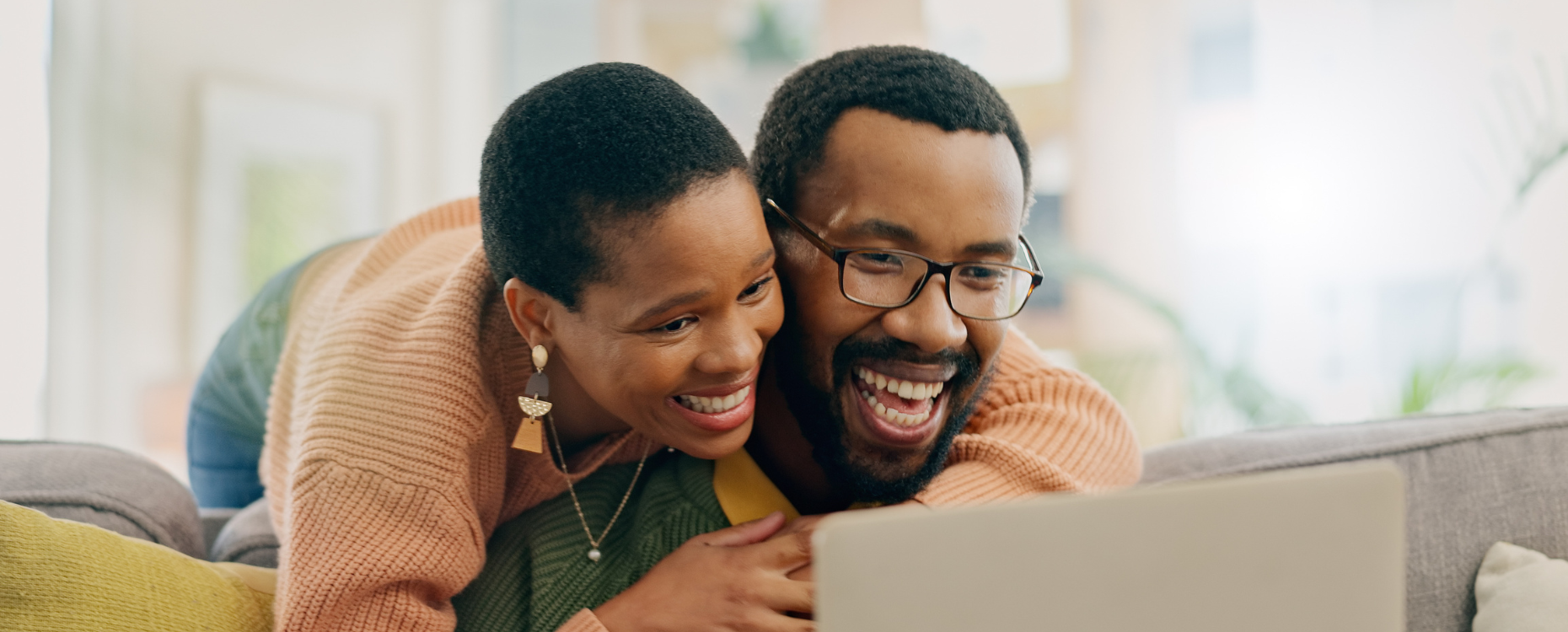 Woman leaning over mans shoulder looking at a laptop and smiling