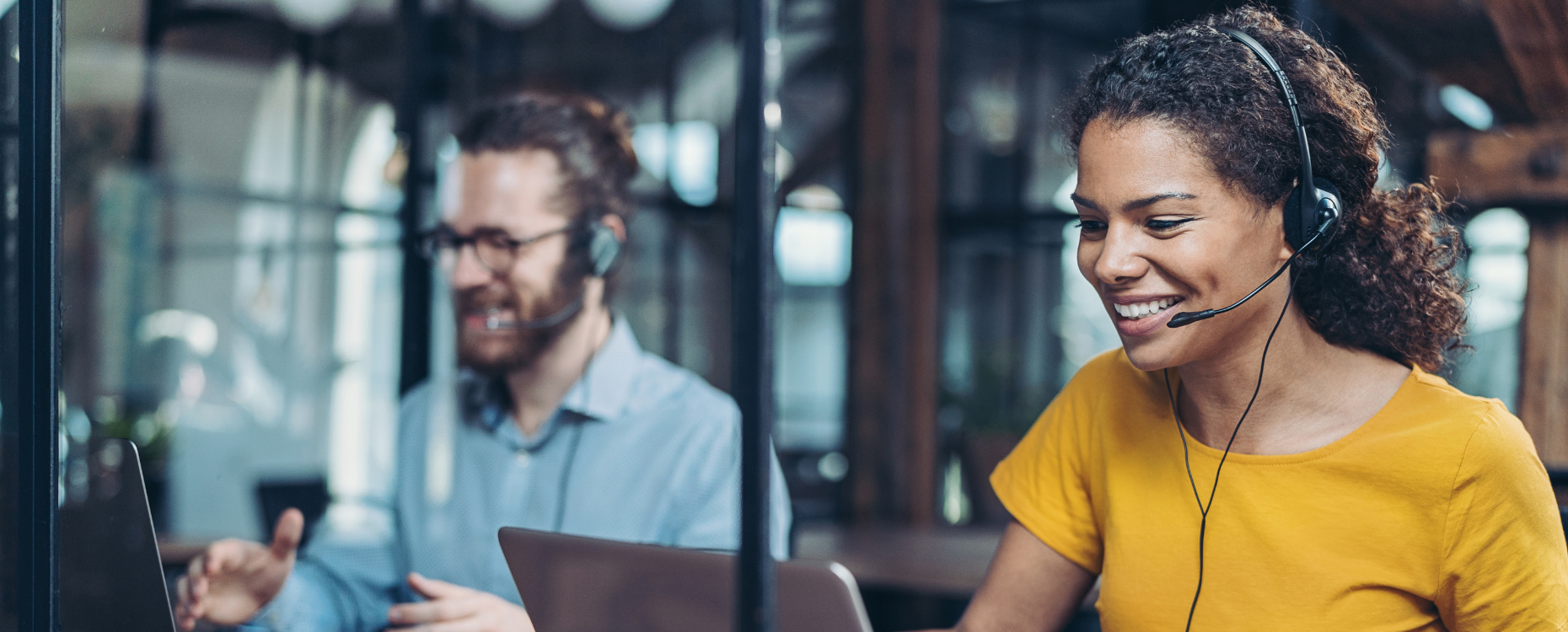 Man and woman wearing headsets talking to customers in front of laptops